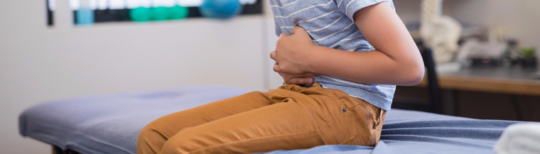 Close-up image of boy clutching his stomach in a doctor's room to illustrate constipation in children.